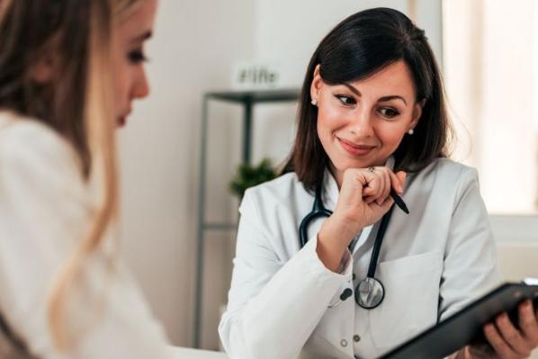 Smiling female doctor talking with another female whilst looking over information on a tablet